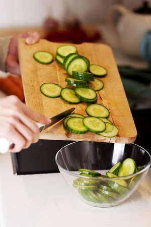 Caucasian attractive young woman is cutting cucumber on kitchen board.の写真素材