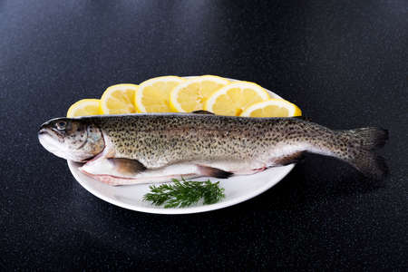 Fresh raw fish lying on a plate with lemon's slices.の写真素材