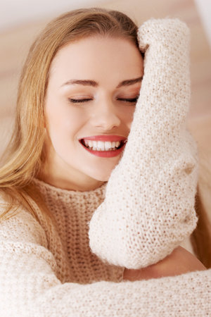 Beautiful caucasian woman is sitting on wooden floor and wearing bright sweater.