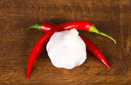 Two chili peppers lying with garlic over wooden background.の写真素材