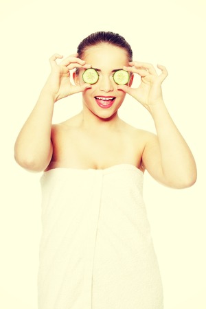 Portrait of the beautyful girl covering her eyes with a slices of a cucumber, isolated on whiteの写真素材