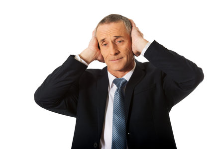 Portrait of tired businessman covering ears with hands.の写真素材