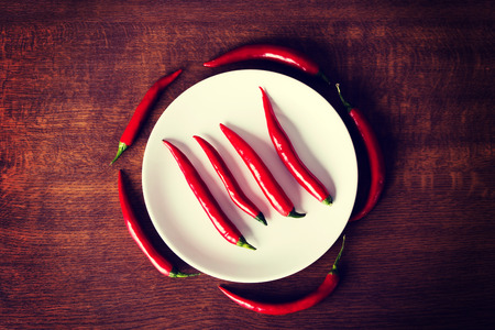 Composition of red chili peppers around white plate.の写真素材