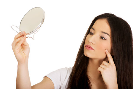 Teenage woman with mirror checking her pimples.の写真素材