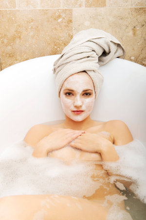 Young spa woman relaxing in bathtub with cream moisturizer.