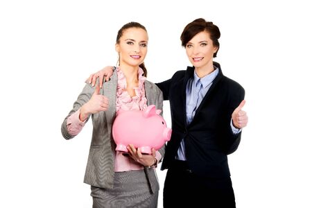 Two businesswoman with thumbs up holding a piggybank.の写真素材