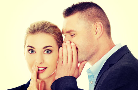 Men whispering secret to his surprised friendの写真素材
