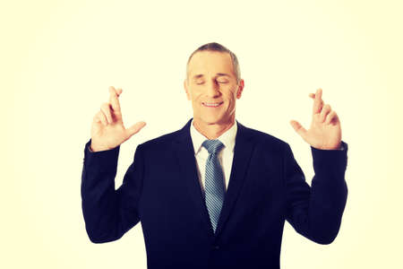 Mature businessman making a wish with fingers crossed.の写真素材