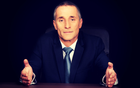 Serious businessman sitting at desk with open hands.の写真素材