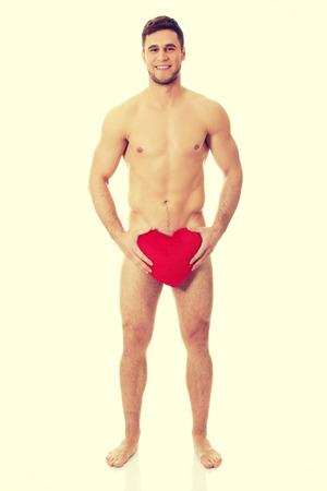 Young handsome nude man covering his self with heart pillow.の写真素材