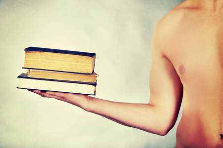 Young shirtless man holding stack of books.の写真素材
