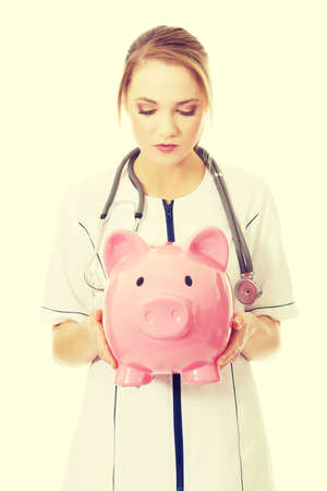 Young beautiful female doctor holding a piggybank.の写真素材
