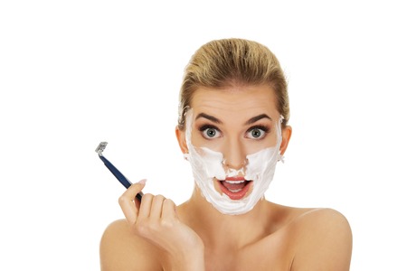Young shocked woman shaving her face with a razor, isolated on whiteの写真素材