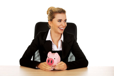 Businesswoman with a piggybank behind the desk.の写真素材