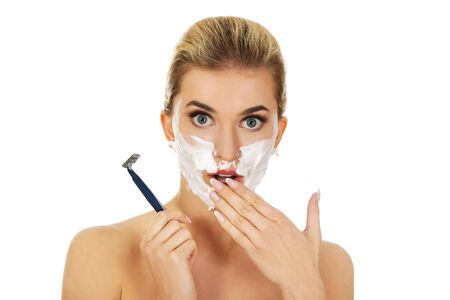 Young shocked woman shaving her face with a razor, isolated on whiteの写真素材