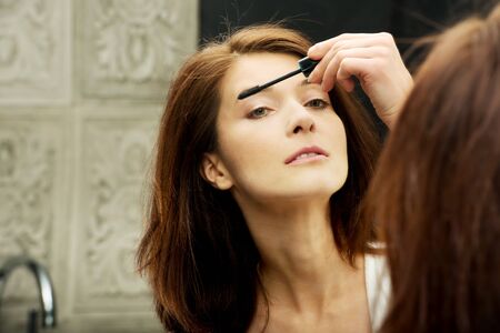 Woman using mascara in bathroom mirror.の写真素材
