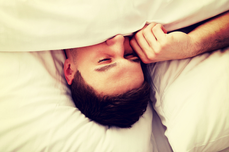 Handsome man rubs his eyes on the bed.の写真素材