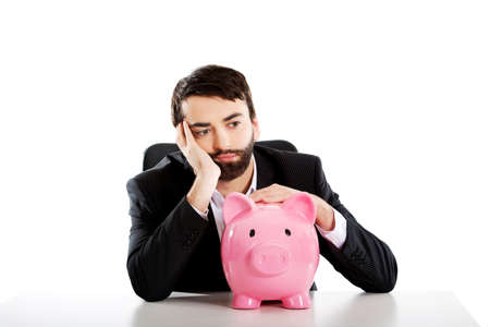 Worried businessman with piggybank by a desk.の写真素材