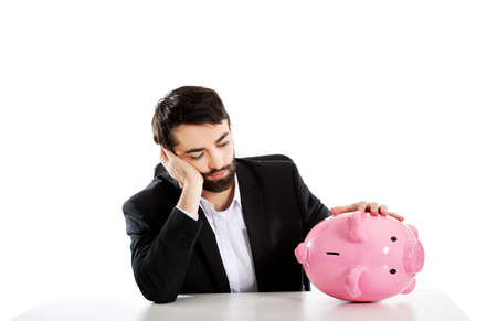 Worried businessman with piggybank by a desk.の写真素材
