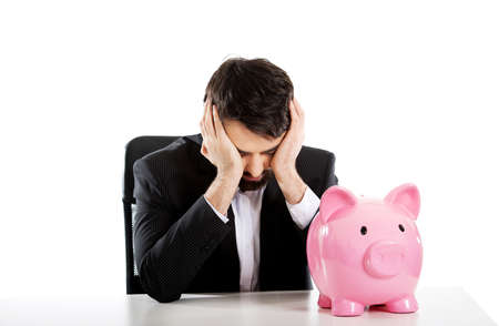 Worried businessman with piggybank by a desk.の写真素材