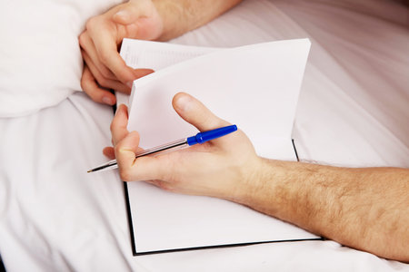 Handsome man writing a note in bed.