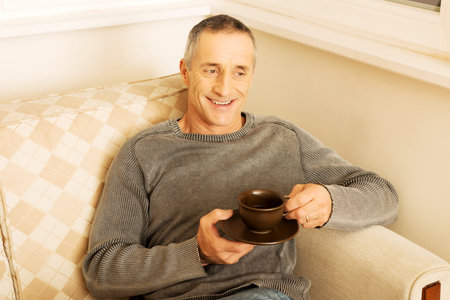 Mature man sitting on couch with cup of coffee.の写真素材