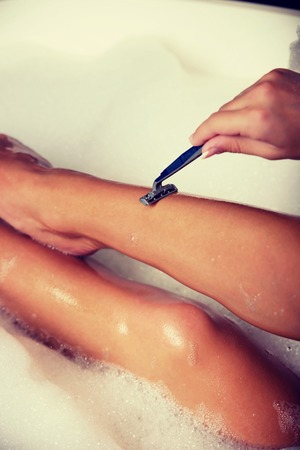 Woman shaving her leg with razor in bathroom.の写真素材