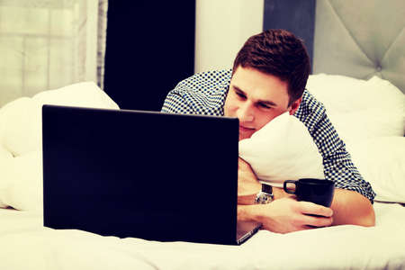 Casual handsome young man using laptop in bed at home.の写真素材