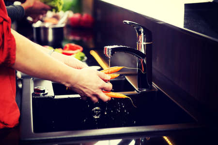 Woman washing carrots in the kitchen sink.の写真素材