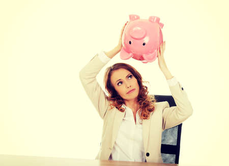 Business woman shaking a piggybank by a desk.の写真素材