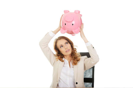 Business woman shaking a piggybank by a desk.の写真素材