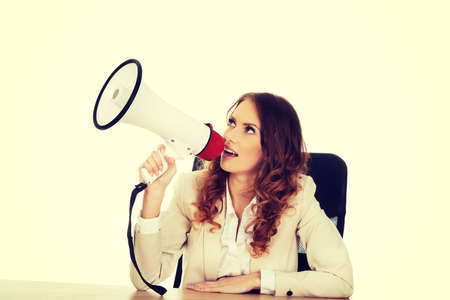 Businesswoman shouting with megaphone by a desk.の写真素材