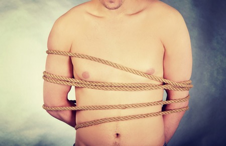 Tortured shirtless man tied with a rope.の写真素材