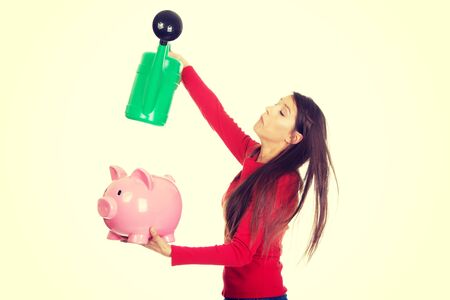 Young woman waters piggybank with watering can.の写真素材