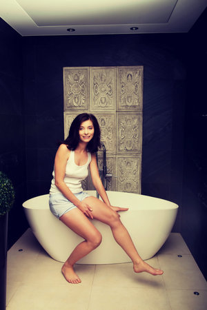 Natural beautiful woman sitting on bathtub in bathroom.
