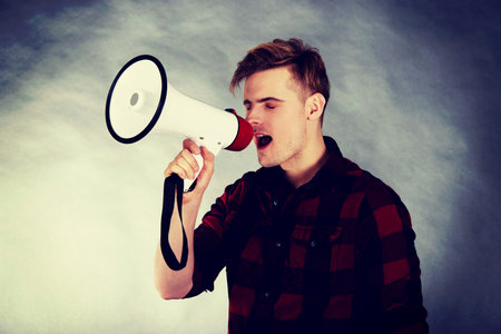 Young handsome man shouting in megaphone.