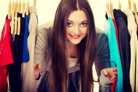 Happy teen woman between clothes on hanger.の写真素材