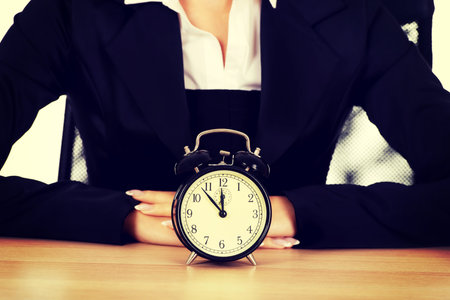 Businesswoman with alarm clock behind the desk.