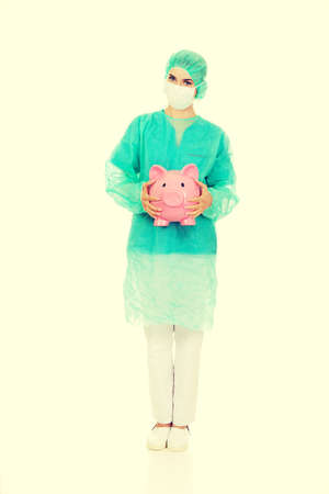 Female surgeon doctor holding piggy bank.の写真素材