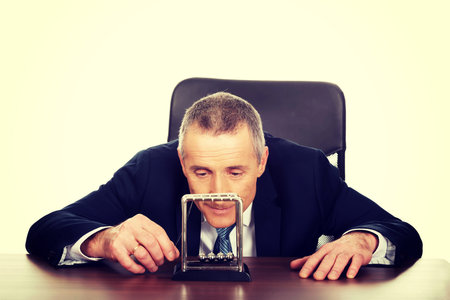 Mature businessman in office playing with newton balls.