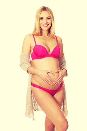 Well groomed pregnant woman making heart shape on bellyの写真素材