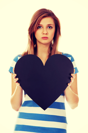 Worried teenage woman holding black paper heart.の写真素材