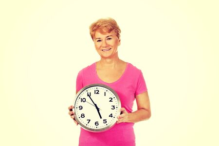 Smiling senior woman holding a clock.の写真素材