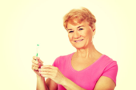 Smiling senior woman holding toothpaste and toothbrush.