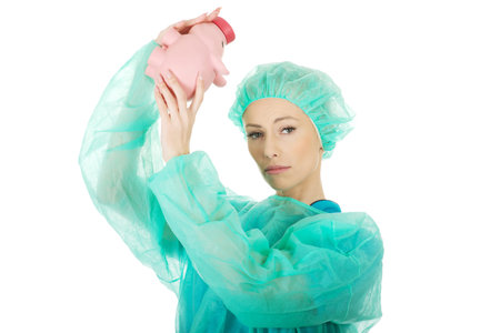 Worried female surgeon doctor with piggy bank.の写真素材