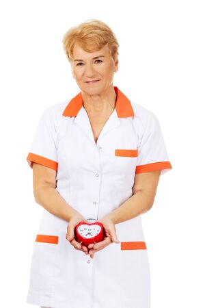 Smile elderly female doctor or nurse holds alarm clock.の写真素材