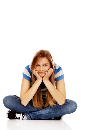 Smiling teenage woman sitting on a floor with legs crossed.の写真素材