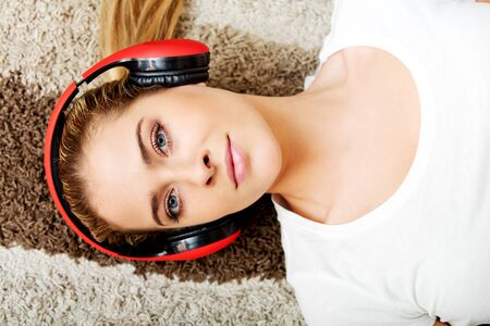Young woman lying on the carpet and listenig a music in headphones.の写真素材