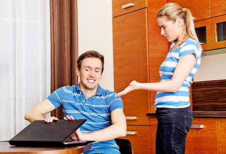 Man watching something on laptop, his wife is angry.