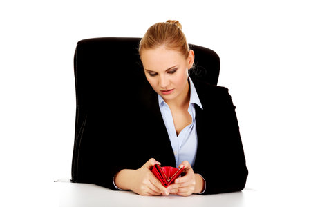 Worried business woman sitting behind the desk with empty wallet.